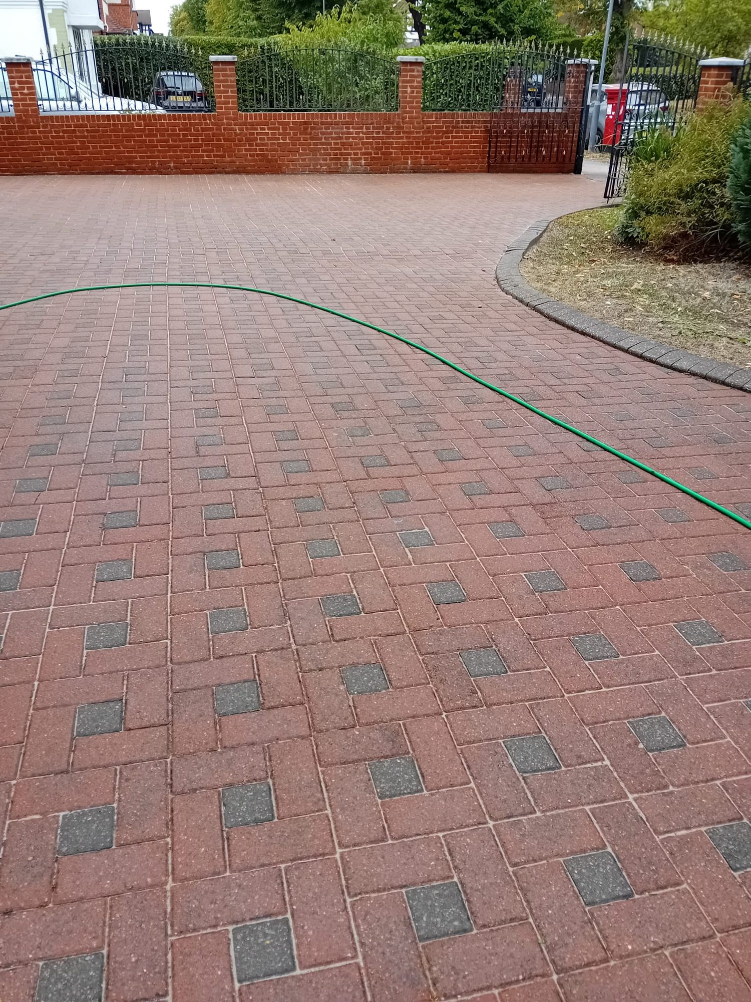 Red block-paved driveway after professional pressure washing, colour restored across the whole surface