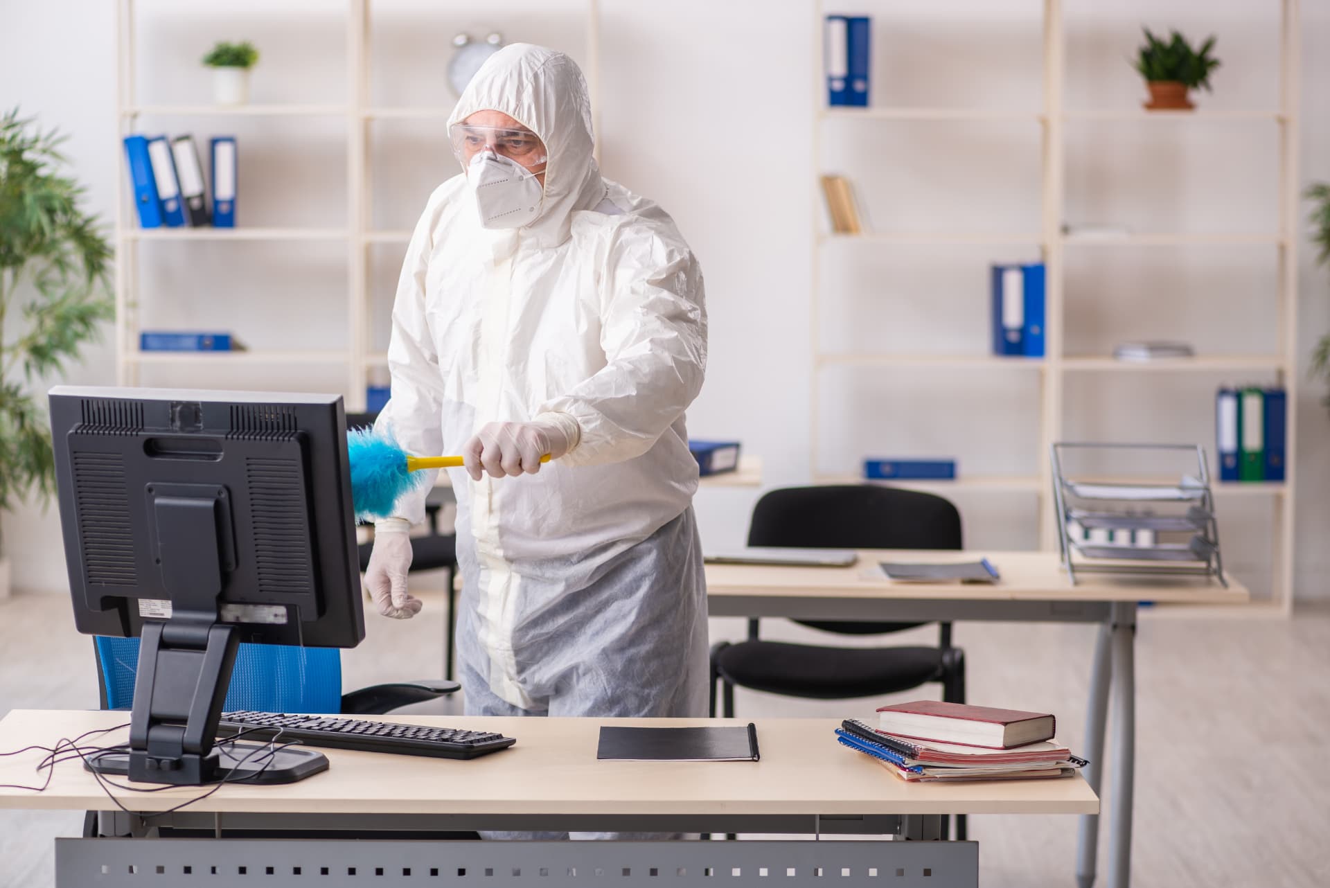 Technician in protective suit sanitising desks and equipment in a commercial office