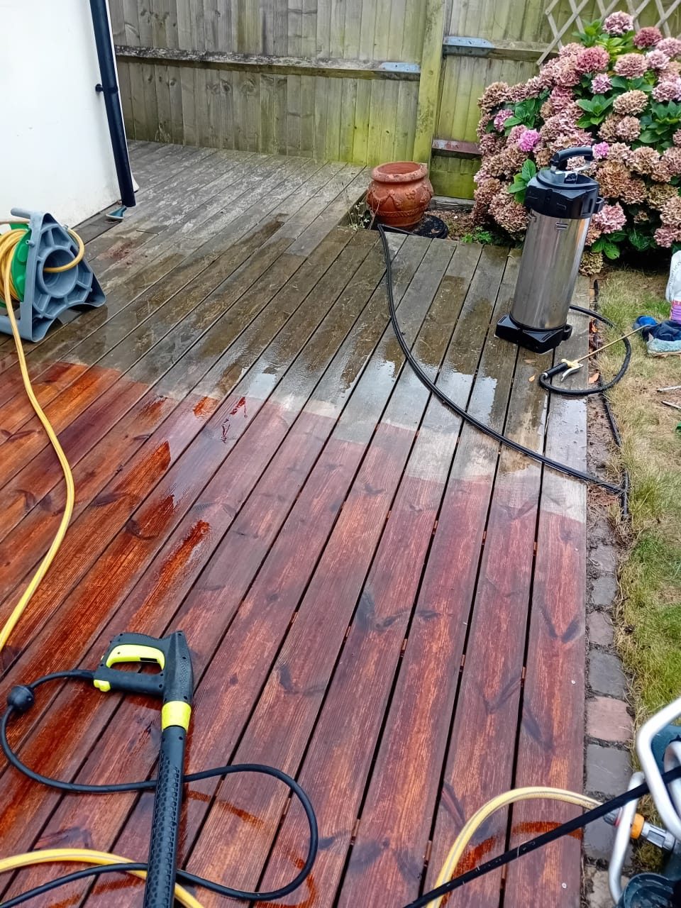 Timber garden decking being pressure washed, the cleaned boards restored to a rich natural colour