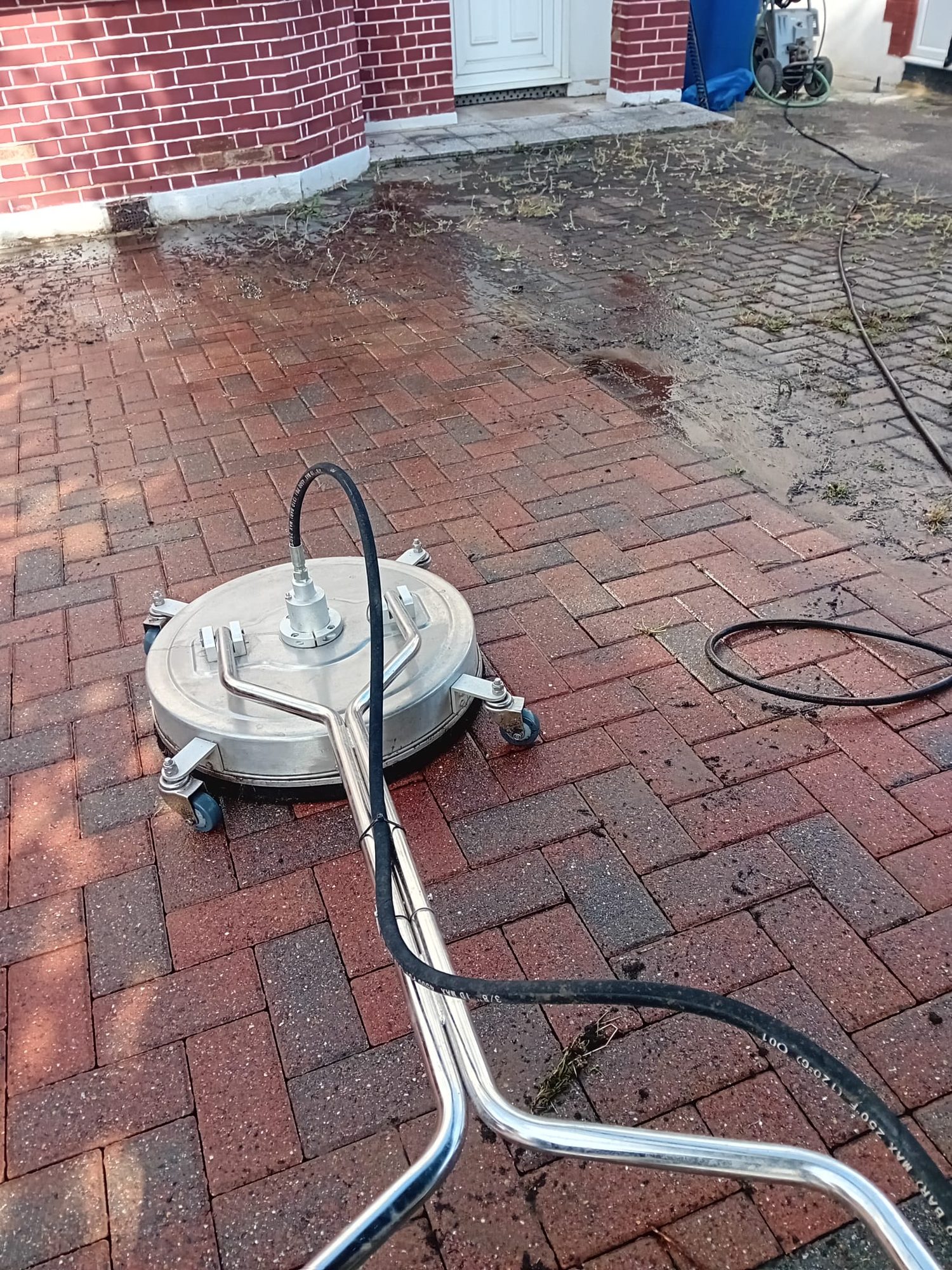 Block-paved driveway cleaned with a rotary surface cleaner, lifting moss and ingrained dirt from the paving