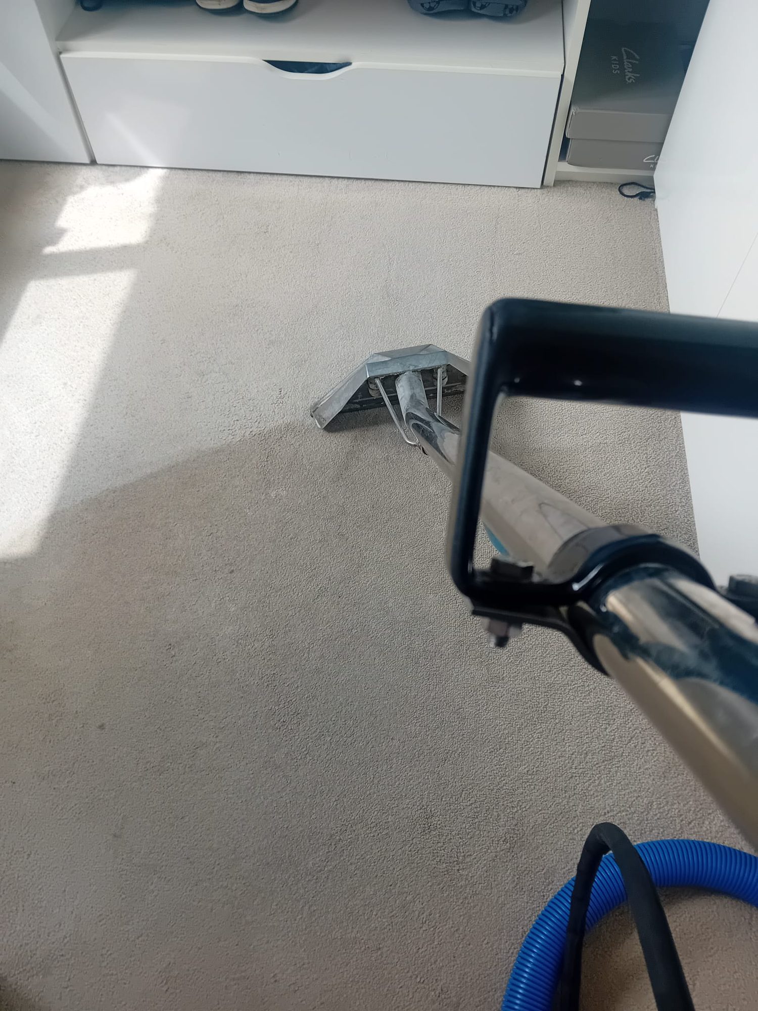 Professional carpet cleaning in progress with a hot-water extraction wand on a cream bedroom carpet